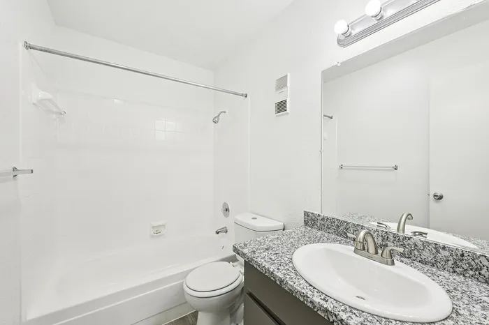 Bright, modern bathroom featuring sleek granite countertop, mirror, and bathtub with elegant tiles.