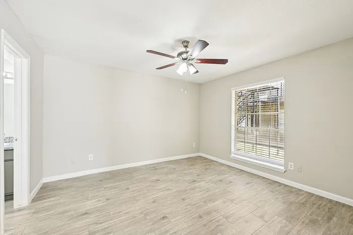 Bright and airy room with modern wood-look flooring, large window, and ceiling fan, perfect for personalization.