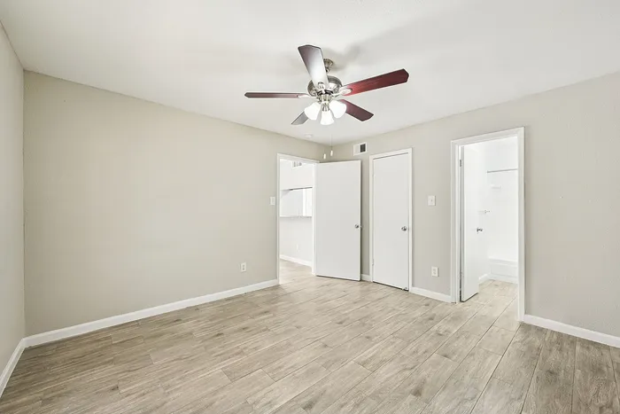 Spacious bedroom with elegant wood flooring, modern ceiling fan, and convenient ensuite bathroom access.
