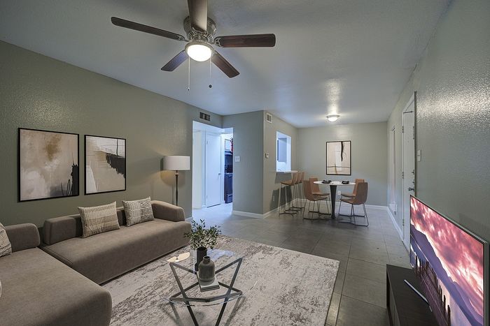 Modern open-plan living room with chic grey tones, stylish wall art, and a cozy seating area, seamlessly connecting to a contemporary dining space with elegant bar stools.