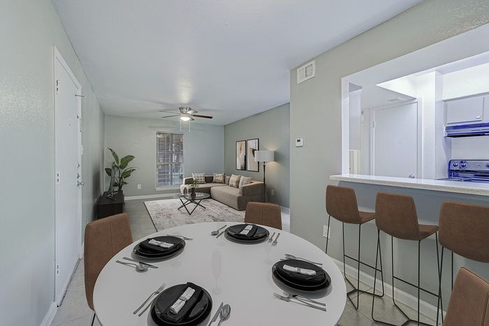 Modern apartment interior showcasing a cozy living room with a stylish sofa and floor lamp, adjacent to a sleek bar counter and inviting dining area with elegant place settings.