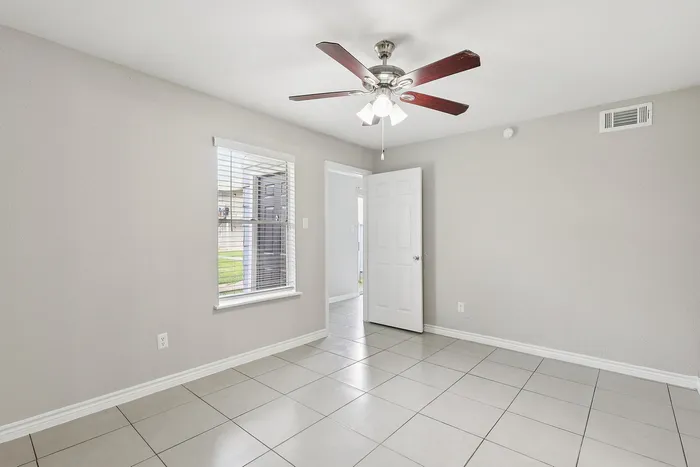 Bright, spacious room featuring elegant tile flooring, modern ceiling fan, and ample natural light from large windows.