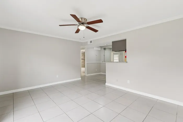 Bright and spacious living area with elegant tiled flooring, a modern ceiling fan, and a sleek open kitchen counter.