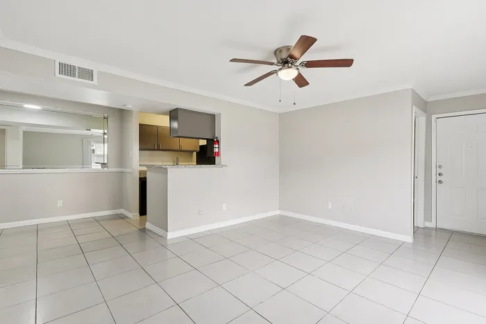Bright open living area with modern ceiling fan and sleek tile flooring, seamlessly connecting to a cozy kitchen with stylish granite countertops.