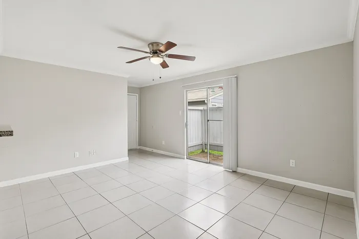 Bright and spacious living area featuring modern tiled floors, a stylish ceiling fan, and inviting sliding glass doors leading to outdoor space.