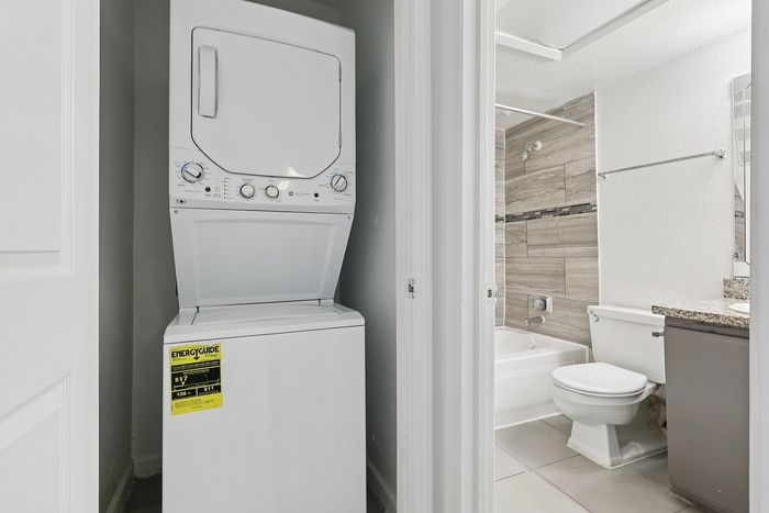 Bright and modern apartment space showcasing an energy-efficient stacked washer and dryer next to a sleek bathroom with elegant tile design.