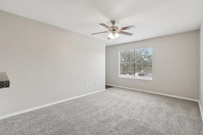 Bright and spacious room with a plush beige carpet, ceiling fan, and a large window inviting natural light.