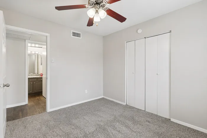 Bright and inviting bedroom featuring plush carpet, ceiling fan, and a glimpse into a modern bathroom with elegant fixtures.