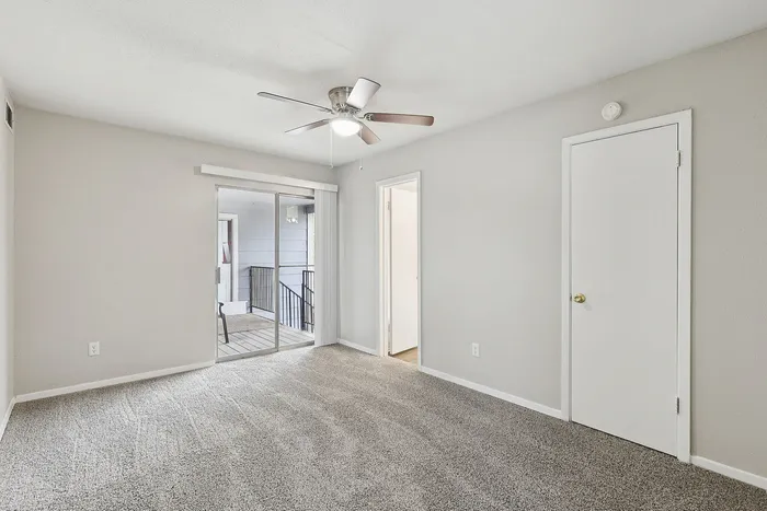 Elegant bedroom with cozy carpet flooring, sliding glass doors leading to a private balcony, and a ceiling fan for comfort.