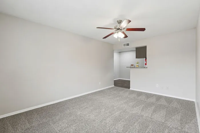 Inviting open-concept living space featuring plush carpeting, an elegant ceiling fan, and a cozy kitchen bar.