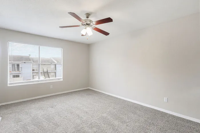 Bright and airy bedroom with plush carpeting, ceiling fan, and a large window offering scenic views, perfect for relaxation.