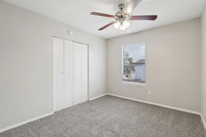 Bright and cozy bedroom with modern ceiling fan, plush carpet, and ample natural light from the window.