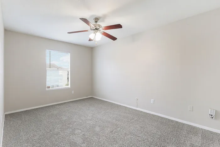 Bright, spacious bedroom with plush carpeting and modern ceiling fan, ideal for creating a cozy personal retreat.