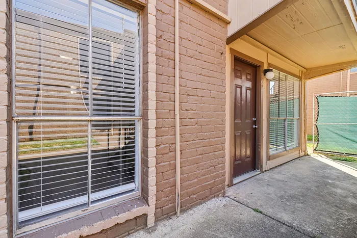 Inviting apartment entrance with charming brick exterior and large sunlit window, ideal for welcoming guests.