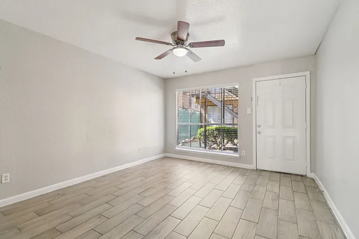 Bright and inviting living area with modern wood tile flooring, large window, and sleek ceiling fan.