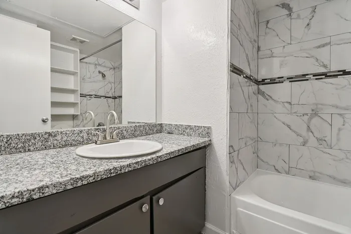 Elegant bathroom featuring a sleek granite countertop, modern sink, and stylish marble-tile shower.