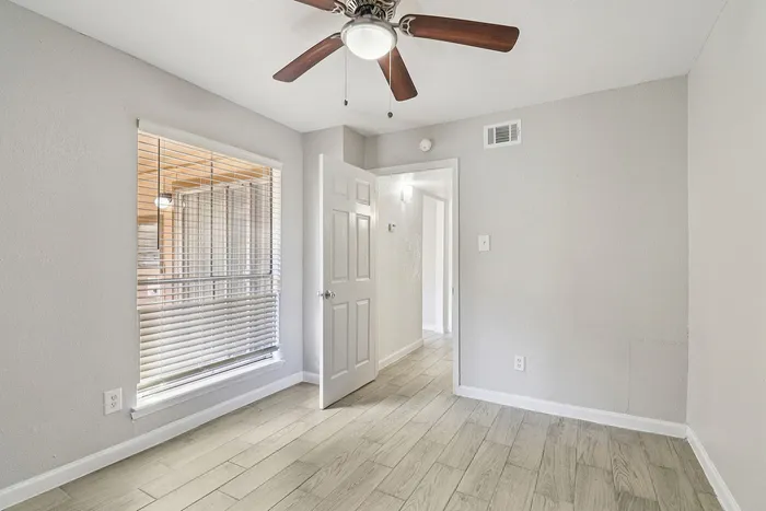Bright room with sleek wood flooring, large window with blinds, and modern ceiling fan offering a cozy ambiance.