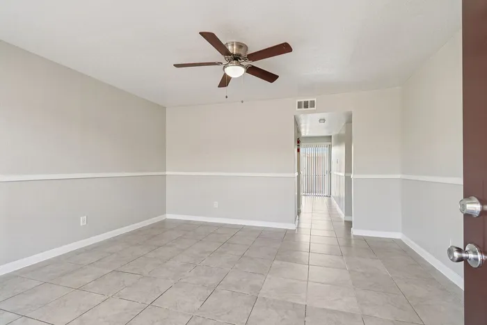 Inviting and spacious living area with elegant tile flooring and a sleek ceiling fan, leading to a naturally lit hallway with stylish vertical blinds.