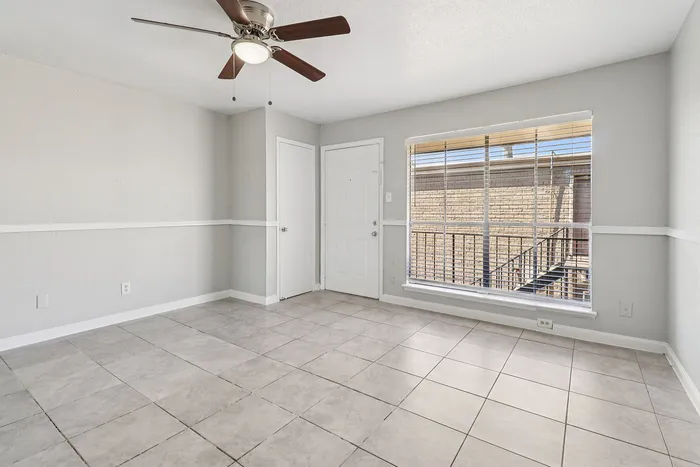 Bright and inviting room with modern tiled flooring, large window with natural light, and sleek ceiling fan.