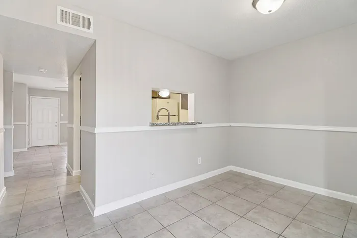 Bright and inviting apartment interior with sleek light gray walls and modern tiled flooring, showcasing an open entrance and accented with a unique kitchen pass-through.
