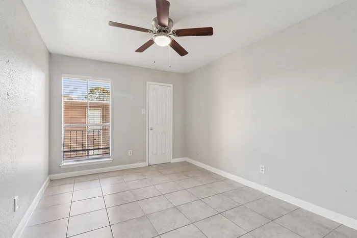 Bright and airy room with elegant tiled flooring, modern ceiling fan, and large window offering ample natural light.