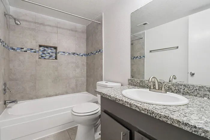 Modern bathroom featuring elegant granite countertops, a pristine bathtub with stylish tile accents, and contemporary fixtures.