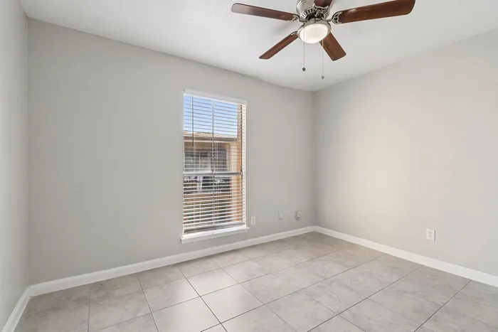 Bright, airy room with sleek tiled flooring and a modern ceiling fan, basking in natural light from a large window with blinds.
