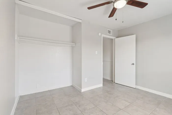 Bright, airy bedroom with modern ceiling fan and spacious closet, featuring elegant tiled flooring.