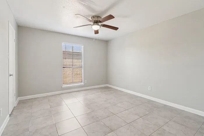Modern, sunlit room with sleek tiled flooring and a ceiling fan, offering versatile space for any style.