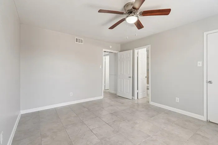 Bright bedroom with modern ceiling fan, elegant tiled floors, and double doors opening to an en-suite bathroom.