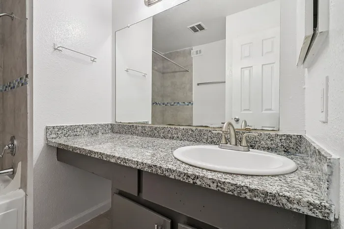 Modern bathroom featuring elegant granite countertops, a sleek faucet, and a large mirror, perfect for a bright and fresh start to your day.