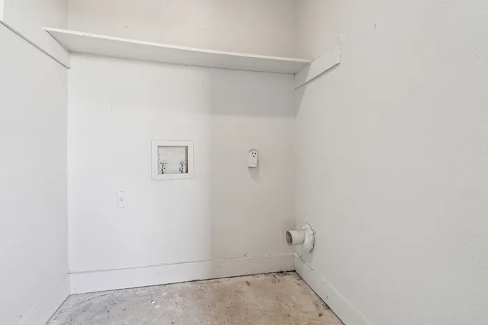Spacious utility room featuring wall-mounted plumbing fixtures and ample storage shelf, perfect for convenient laundry setup.