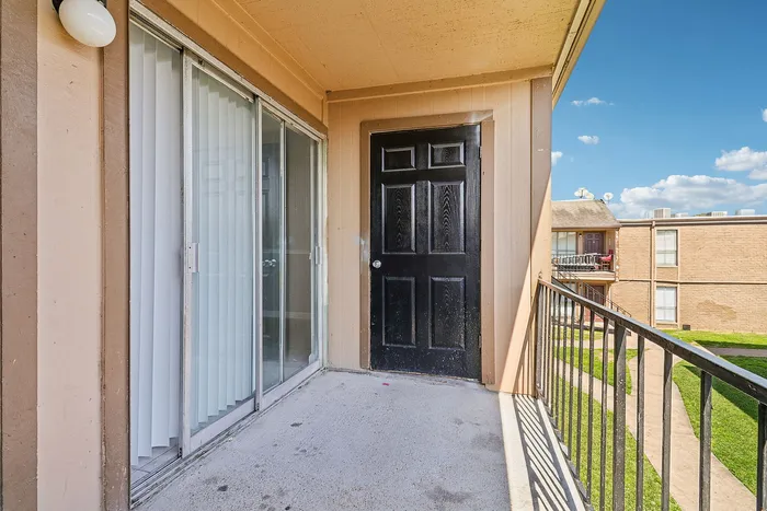 Charming apartment balcony with a sleek black door, sliding glass doors, and a sunny view of the well-maintained courtyard.
