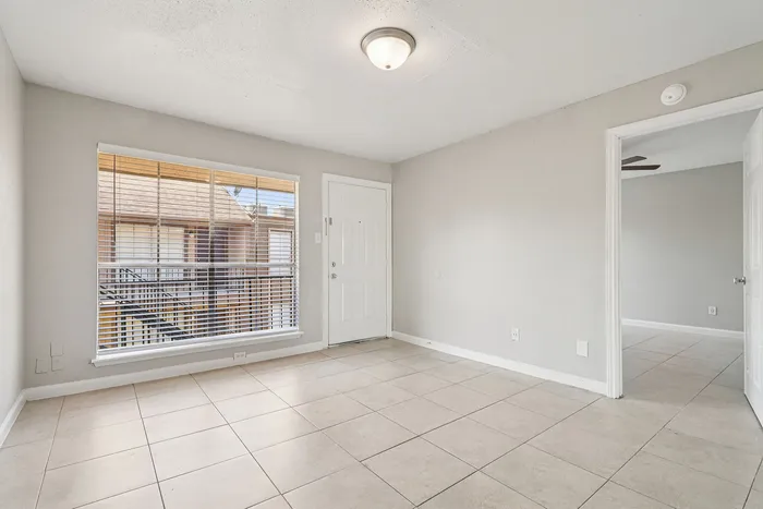 Bright, inviting room with neutral-toned ceramic tile flooring, large window offering natural light, and access to an adjoining space.