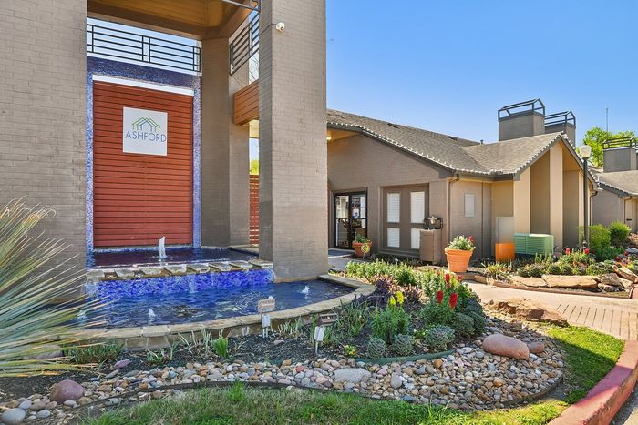 Charming apartment entrance with a serene water feature, vibrant landscaping, and modern architecture at Ashford.