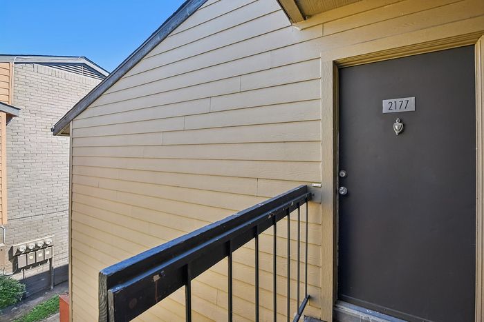 Inviting apartment entrance with a sleek black door, accented by charming wood siding and modern railing.
