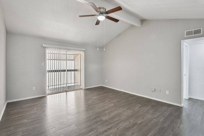 Bright living room with sleek wooden floors, large sliding glass doors, and modern ceiling fan.