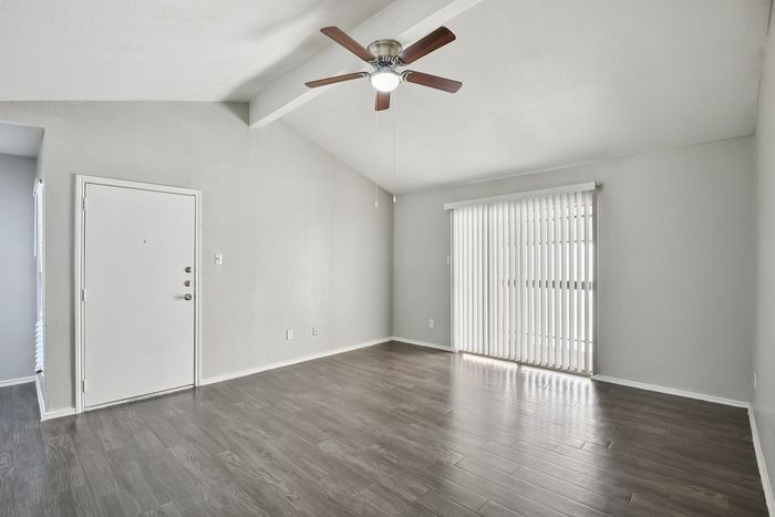 Elegant living space featuring modern gray flooring, a ceiling fan, and abundant natural light through vertical blinds.