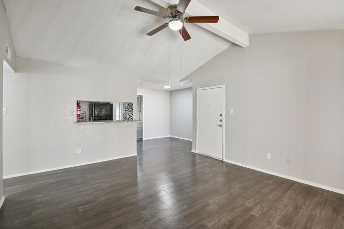 Spacious open living area with elegant wood flooring and modern ceiling fan, leading into a stylish kitchen with granite countertops.