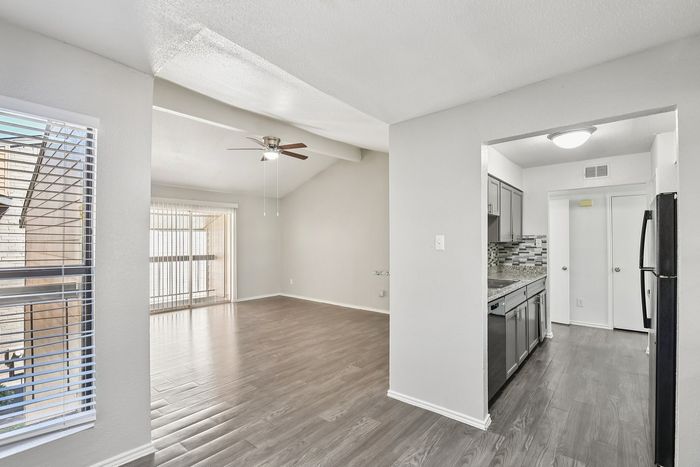 Bright open-plan apartment with sleek hardwood floors, modern kitchen, and ceiling fan, flooded with natural light from large windows.