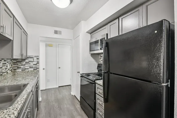 Modern kitchen with sleek black appliances, elegant granite countertops, and stylish gray cabinetry complemented by mosaic tile backsplash.