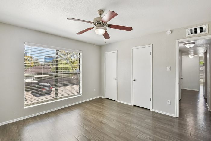 Bright and airy room with elegant wooden flooring, large window, and modern ceiling fan, offering a serene view of the neighborhood.