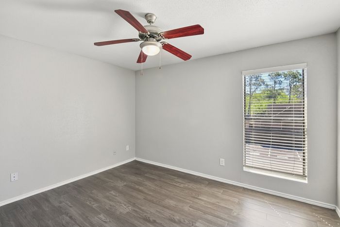 Bright bedroom with sleek hardwood floors, large window, and modern ceiling fan.