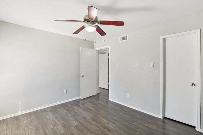 Bright, airy bedroom with elegant wood flooring and modern ceiling fan, offering a fresh and inviting atmosphere.