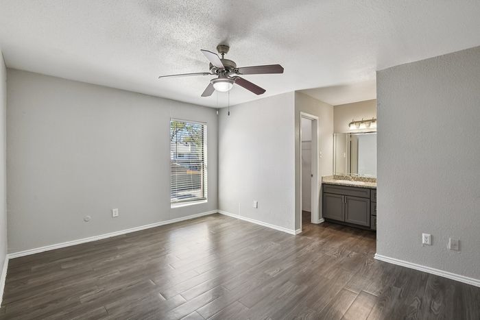 Bright and airy bedroom with sleek hardwood flooring and a modern ceiling fan, leading to an elegant bathroom vanity area.