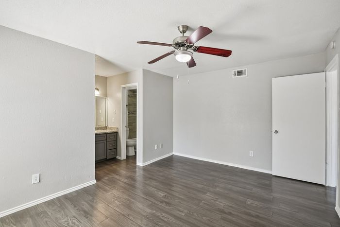 Modern living space with elegant wood flooring, ceiling fan, and access to a sleek ensuite bathroom.