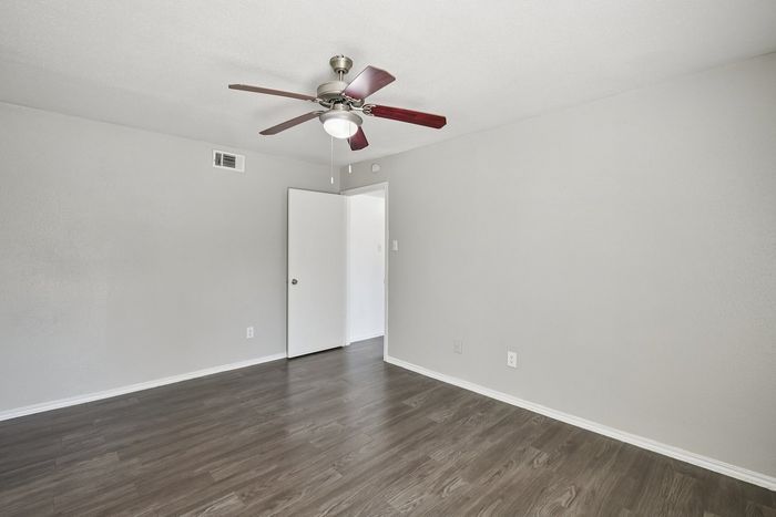 Bright, spacious room with sleek hardwood floors, modern ceiling fan, and clean white walls.