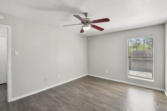 Bright room with sleek hardwood floors, modern ceiling fan, and large window revealing lush outdoor view.