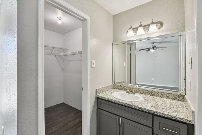 Elegant bathroom with granite countertop and spacious walk-in closet, offering modern lighting and sleek cabinetry.