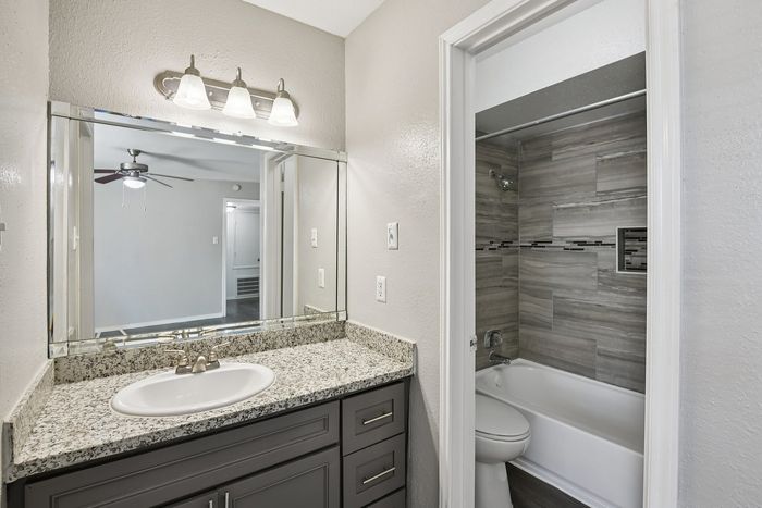 Modern bathroom featuring a granite countertop, sleek vanity, and elegant lighting adjacent to a stylish tiled shower.
